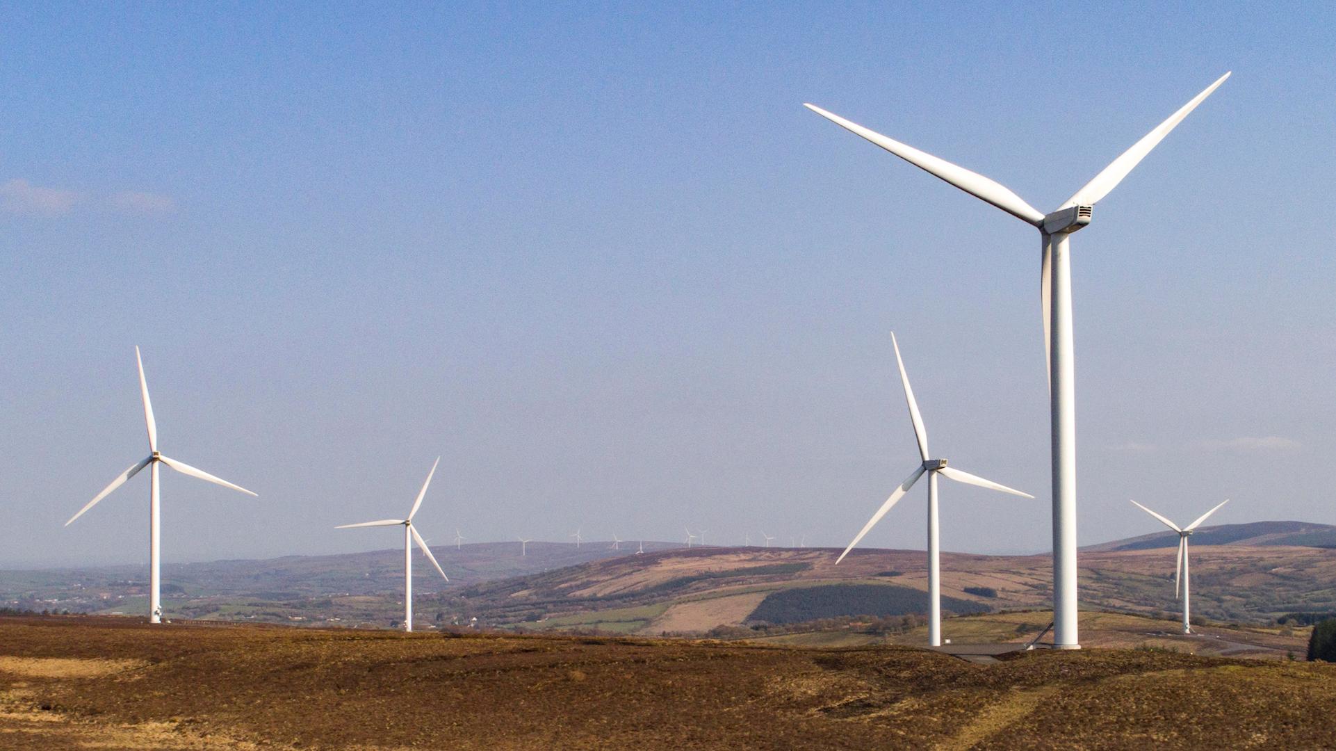 Onshore wind farm with multiple wind turbines operating across a hilly rural landscape under a clear blue sky