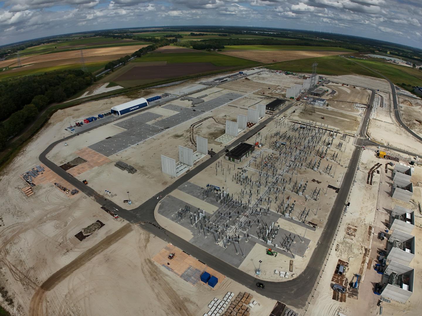 Wide aerial view of a large electrical substation under construction with switchgear foundations and transmission infrastructure in a rural landscape