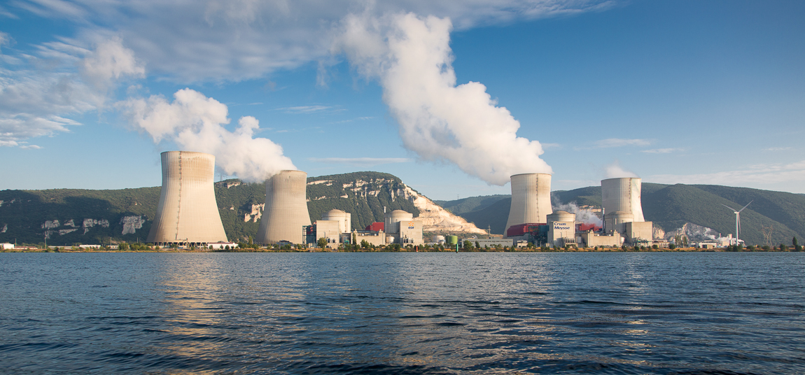 Nuclear power station beside a lake with multiple cooling towers releasing steam, highlighting lowcarbon electricity production