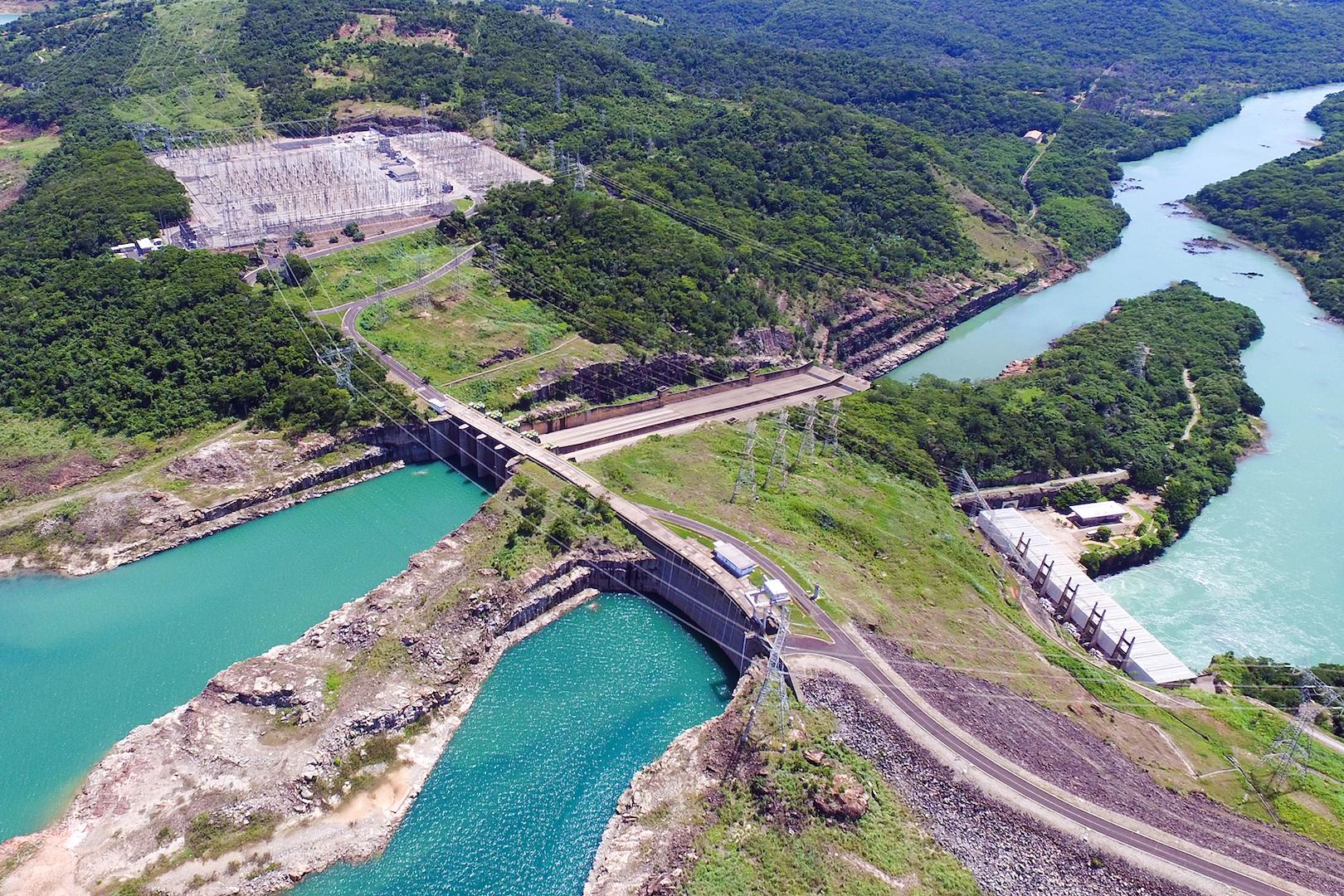 Aerial view of the Emborcação hydroelectric power plant in Brazil, showing the dam, spillway, reservoir, and transmission infrastructure integrated into a green mountainous landscape for renewable energy generation.