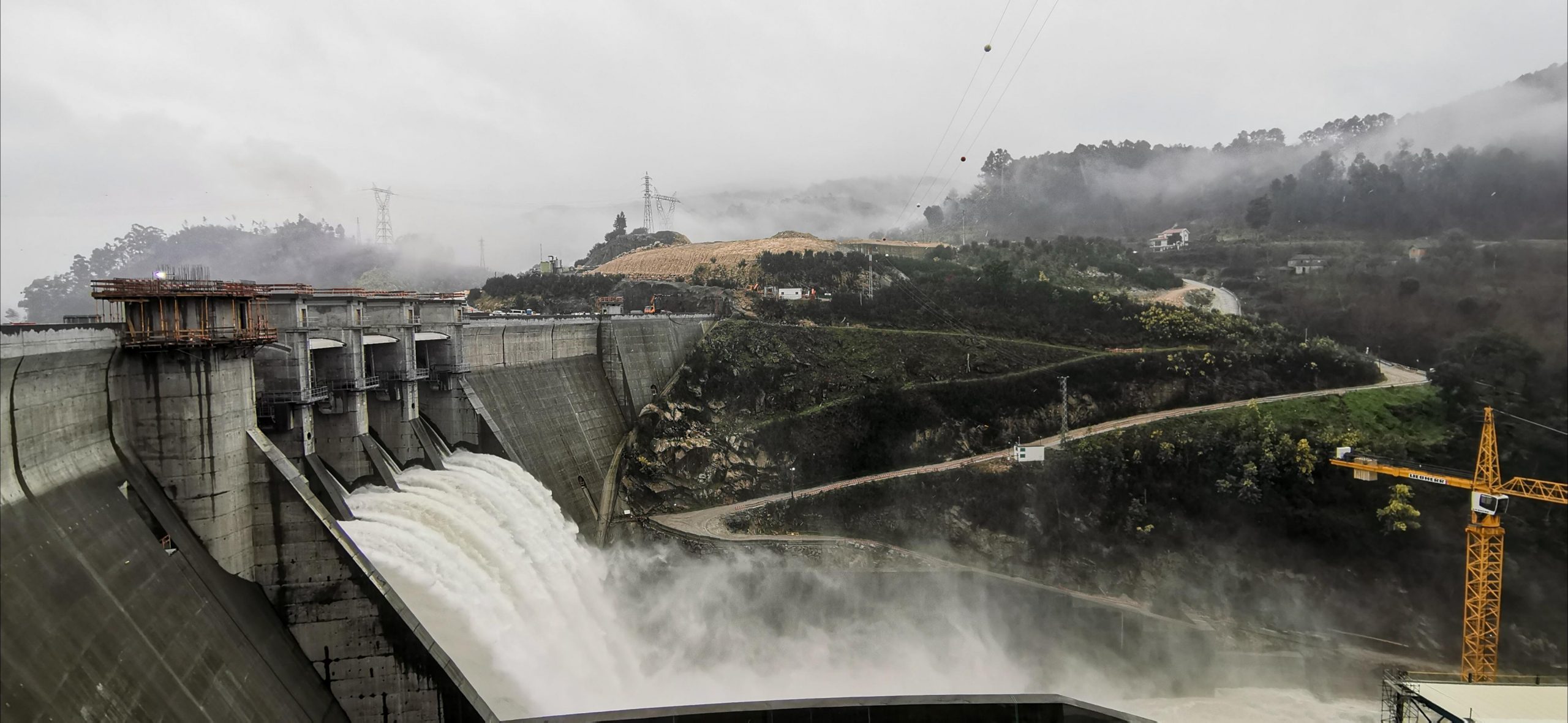 Hydroelectric power plant dam in Portugal releasing water through spillways, showcasing large-scale renewable energy infrastructure by Omexom in a mountainous landscape.