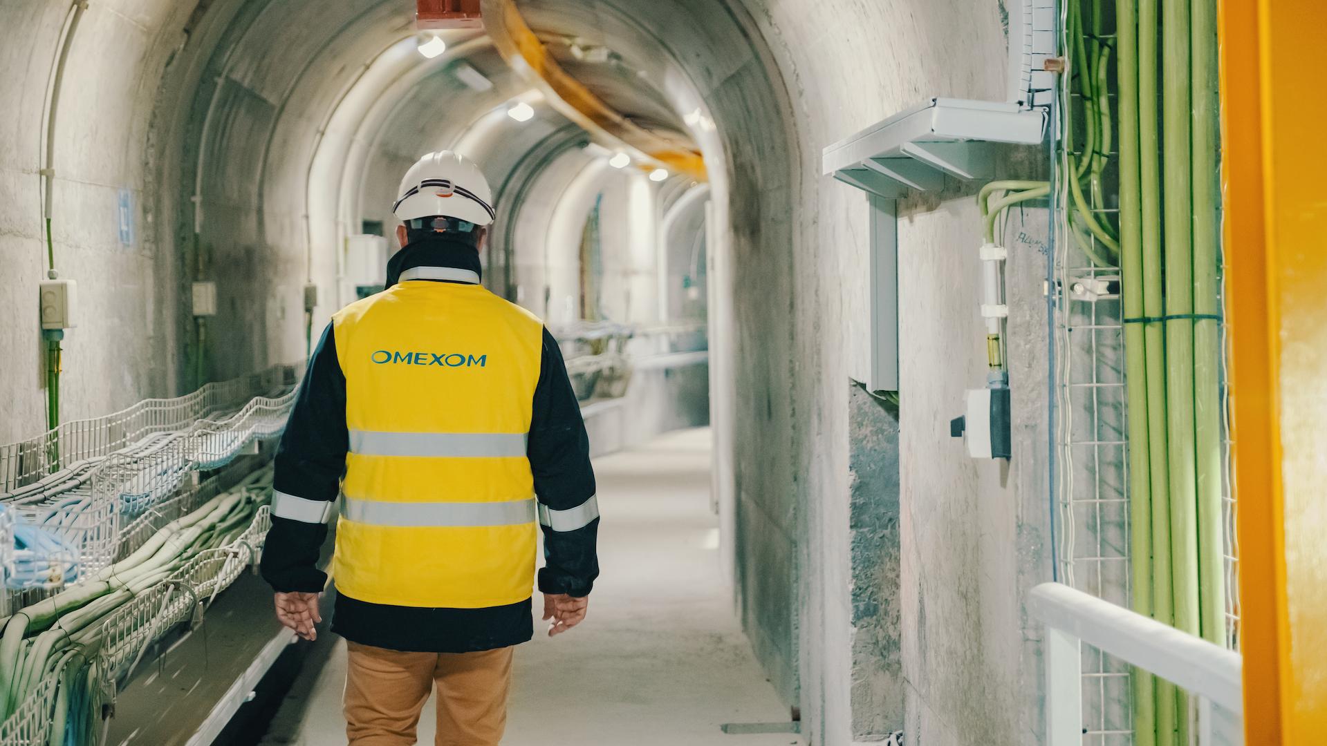 Omexom engineer walking through underground tunnel at a hydroelectric power plant, inspecting electrical cabling and infrastructure for renewable energy production in Portugal.