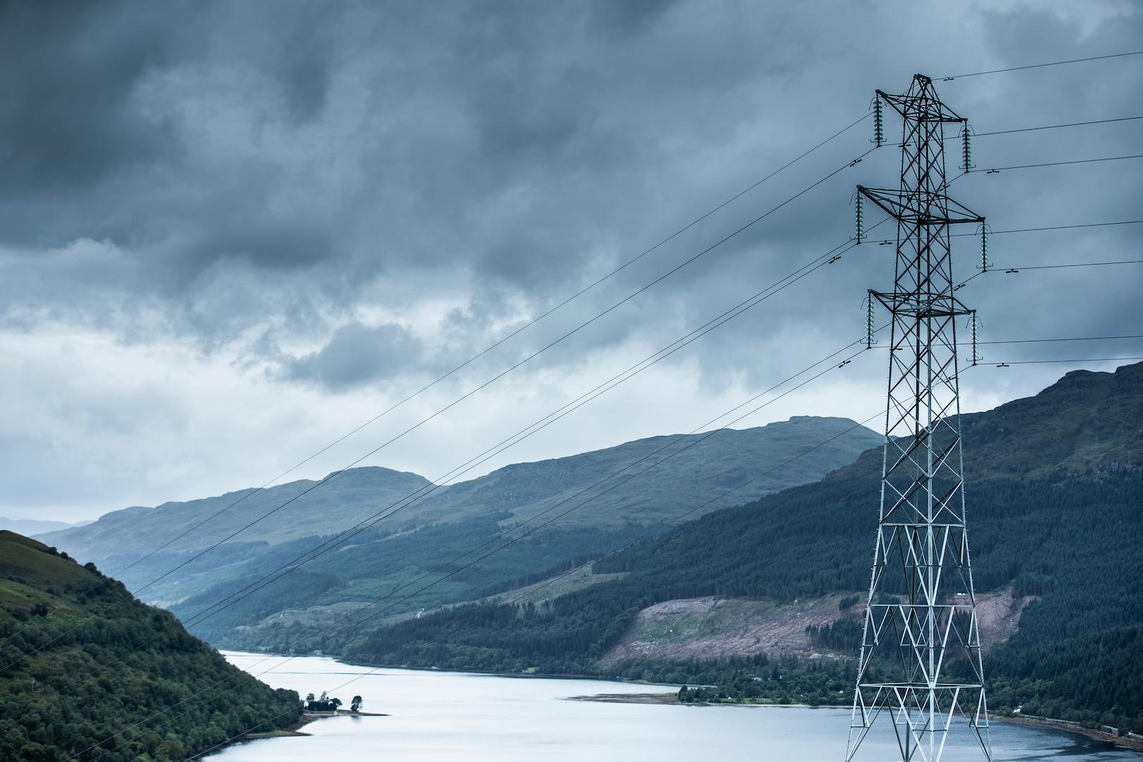High-voltage transmission tower and conductors spanning across a mountainous lake landscape