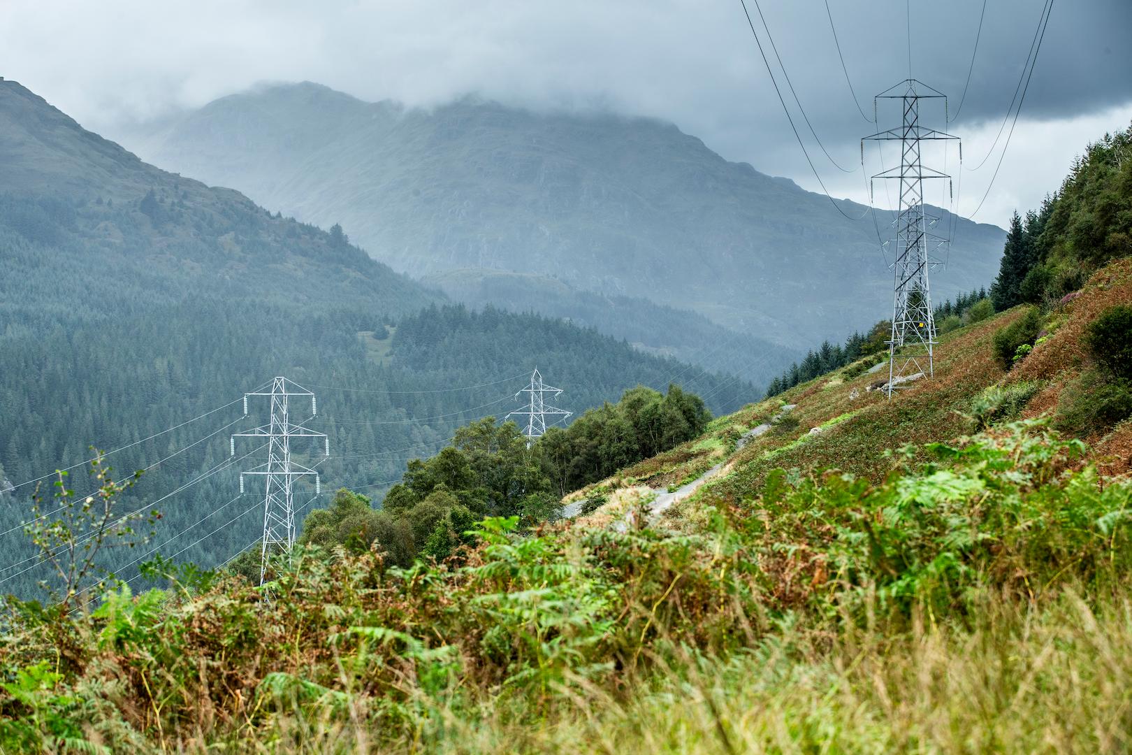 Overhead power transmission towers integrated into a mountainous landscape with dense vegetation