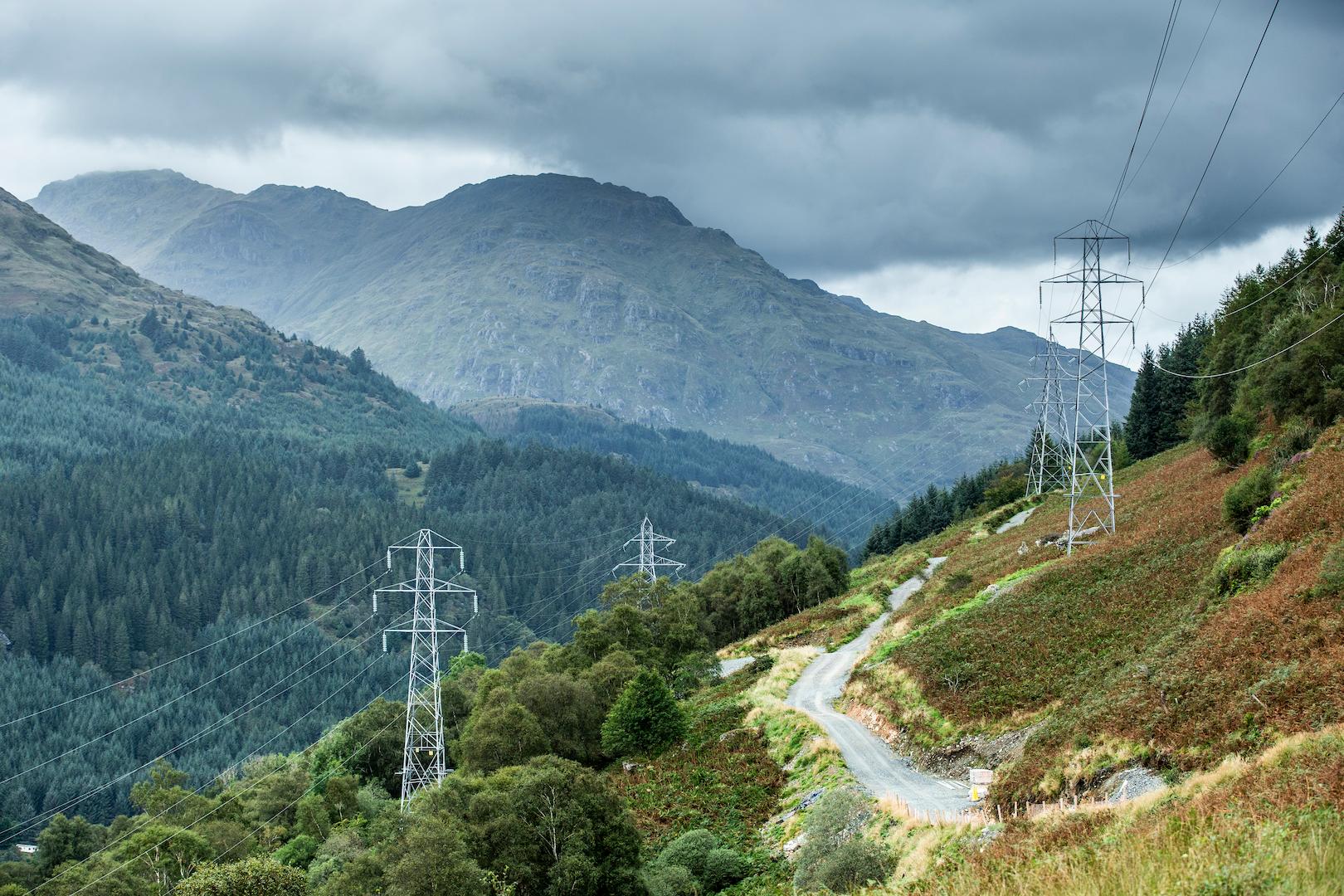 Highvoltage transmission pylons following a mountain access road through forested terrain