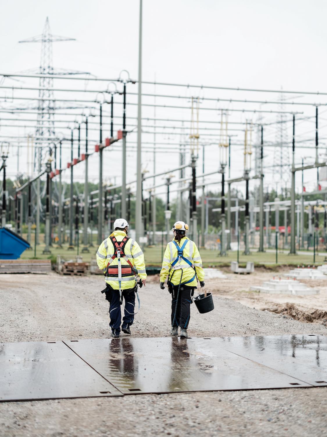 Two electrical technicians inspecting substation structures and overhead power lines on site