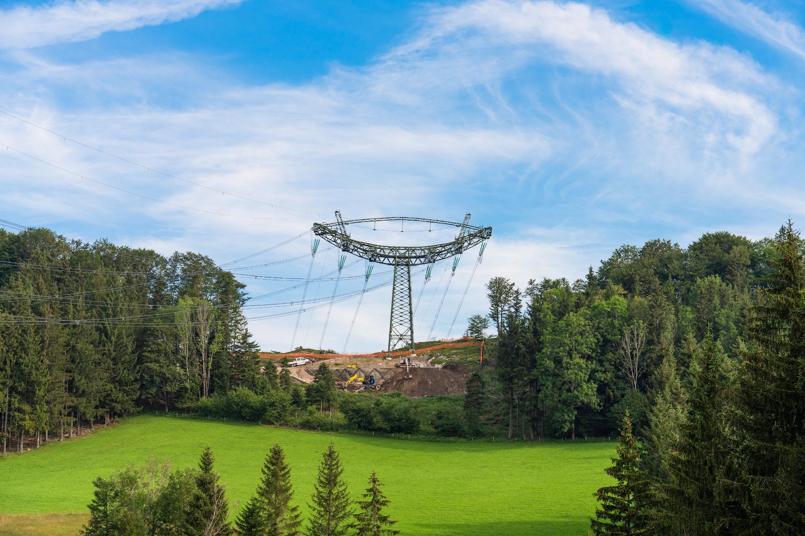 High-voltage transmission tower installed in a forested and agricultural landscape