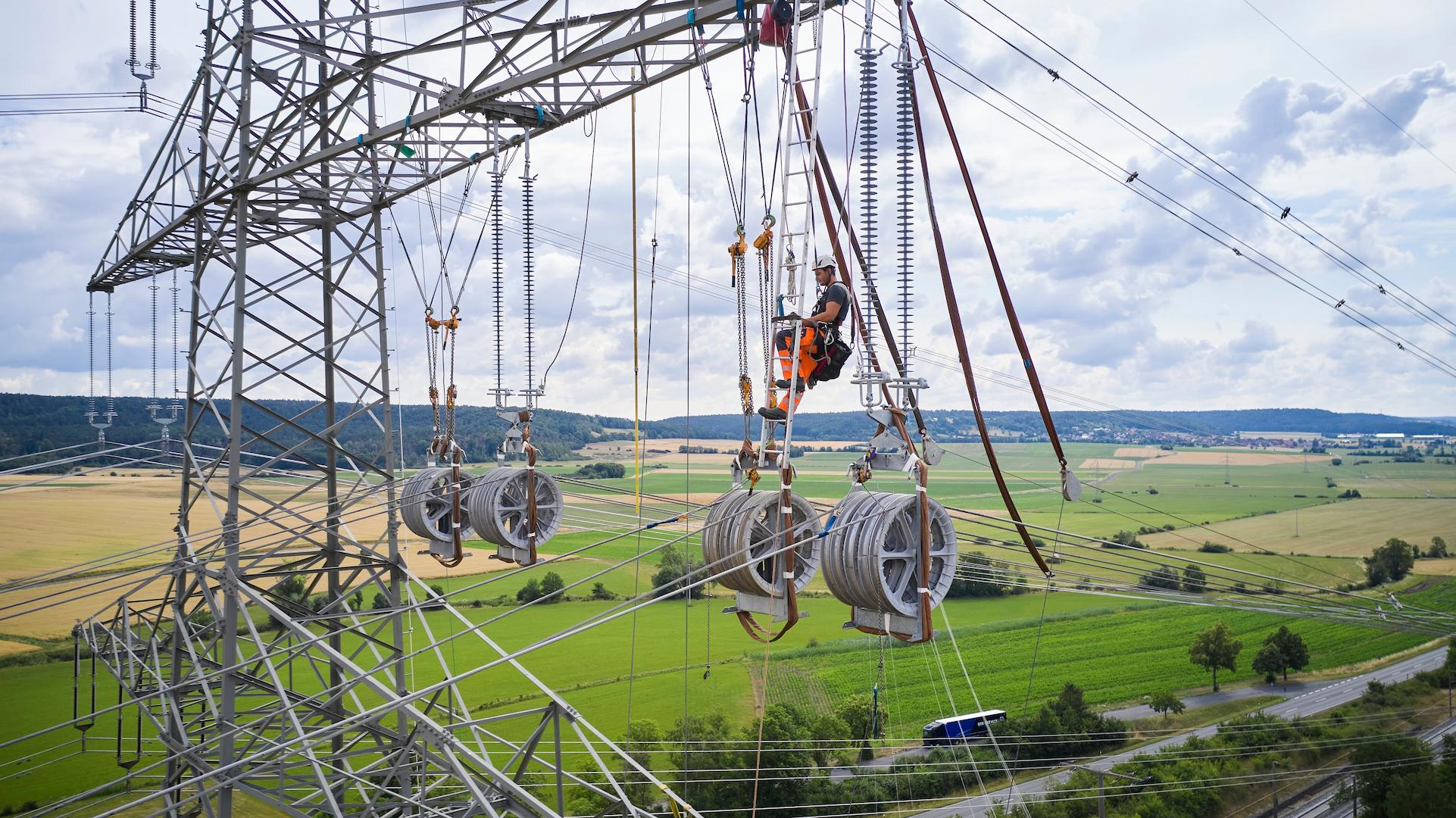 High-voltage transmission line installation on a pylon using suspended conductor reels above open countryside