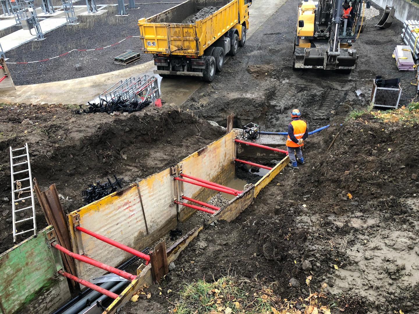 Excavator performing precise trench excavation for underground power transmission cables during electrical infrastructure construction