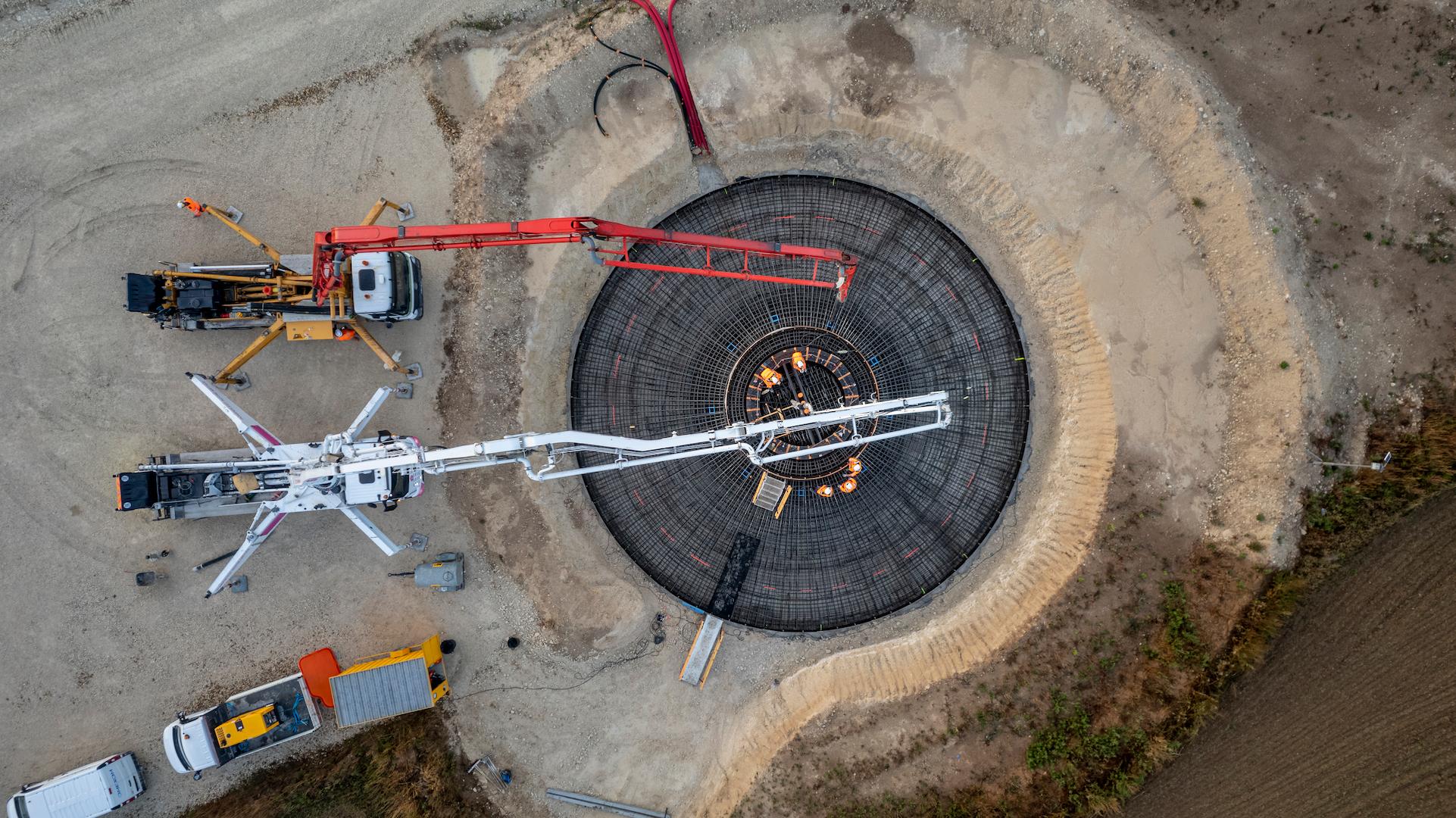 Topdown aerial view of a circular wind turbine foundation under construction with cranes and reinforcement steel