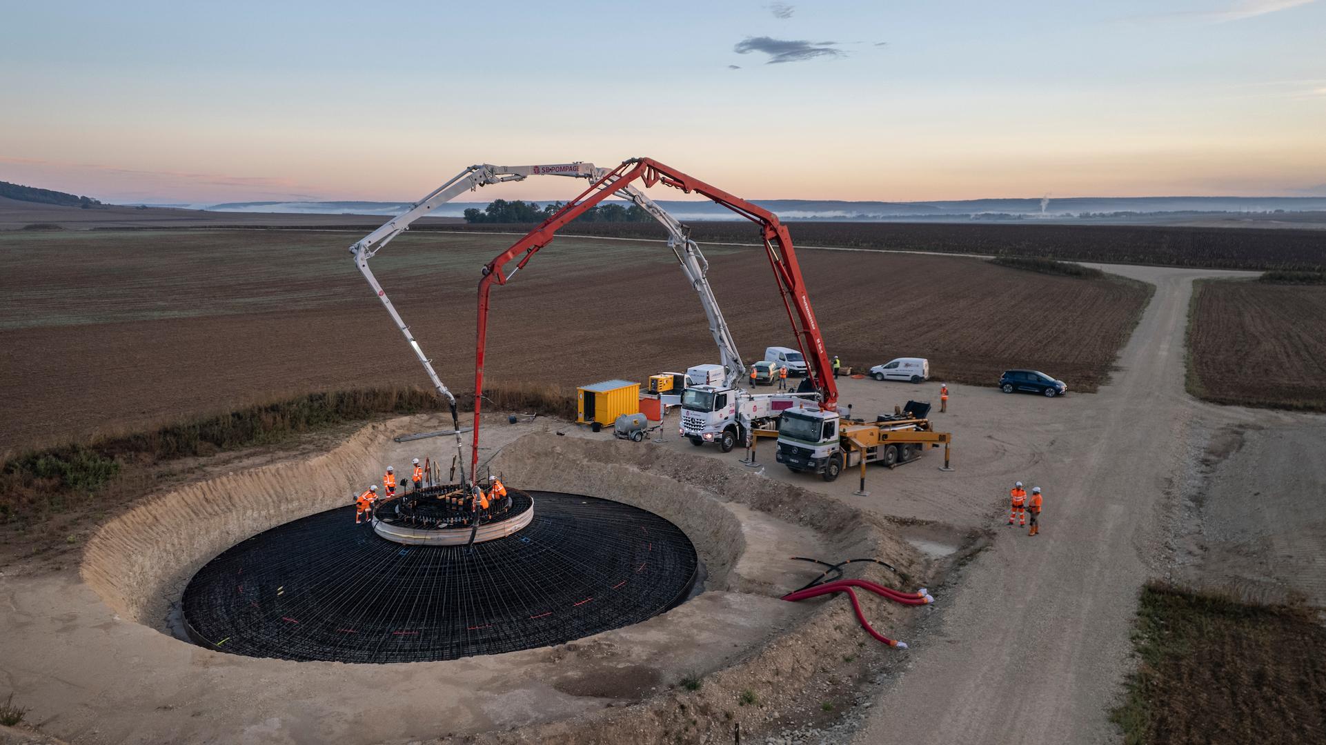 Wind turbine foundation construction site with concrete pouring and heavy machinery in an agricultural area
