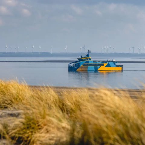 Electric catamaran E-Kat sailing along dune coastline