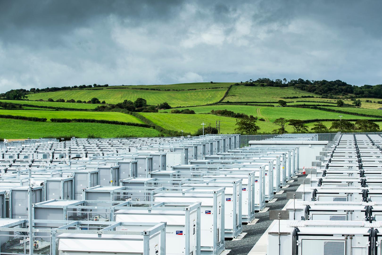 Largescale battery energy storage system installation in a rural landscape with rows of white storage units.