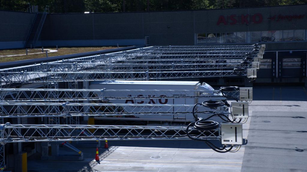 Large-scale electric vehicle charging dock infrastructure with multiple overhead charging arms installed in a logistics and parking facility