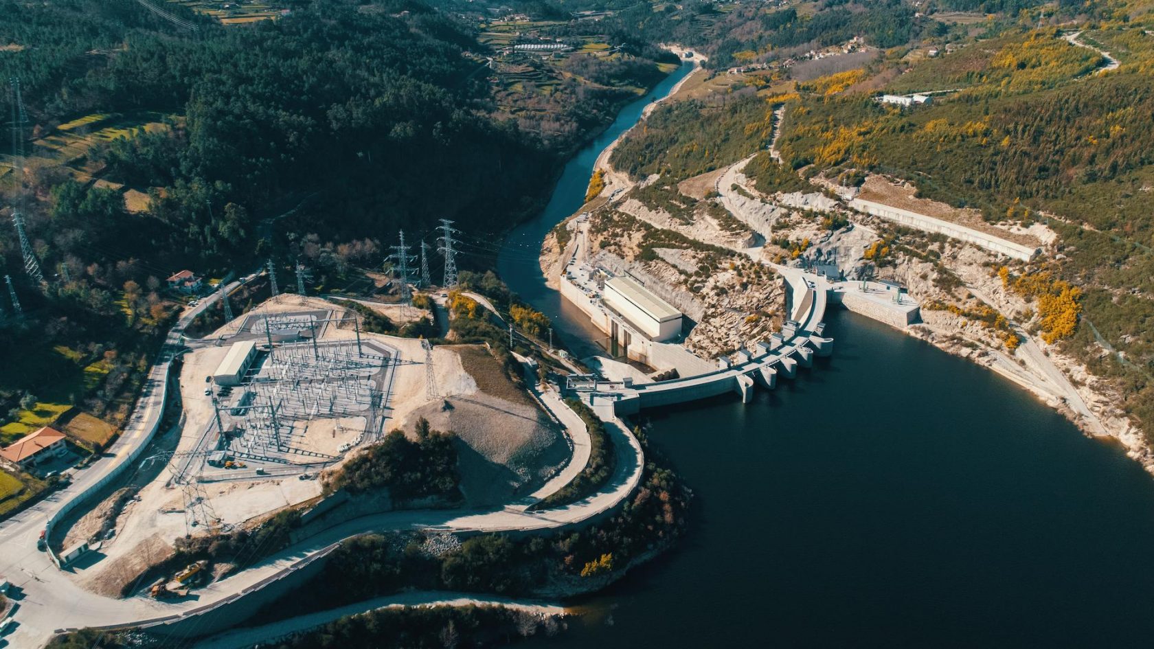 Aerial view of a hydroelectric power plant, dam, and reservoir located in a mountainous landscape.