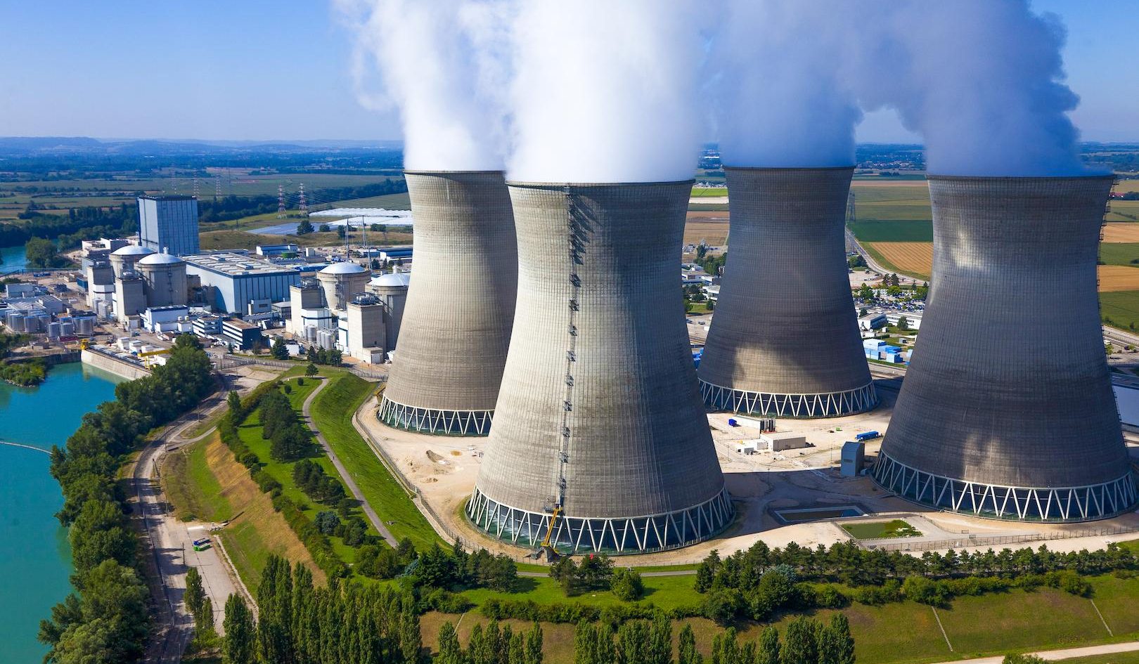 Aerial photo of a nuclear power plant with cooling towers emitting steam next to a river.