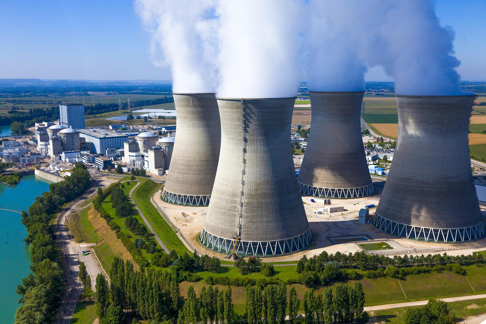 Aerial photo of a nuclear power plant with cooling towers emitting steam next to a river.