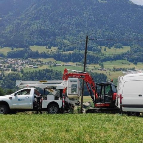 Utility vehicles and machinery positioned in a mountainous landscape for overhead power line installation and electricity distribution works in a rural region