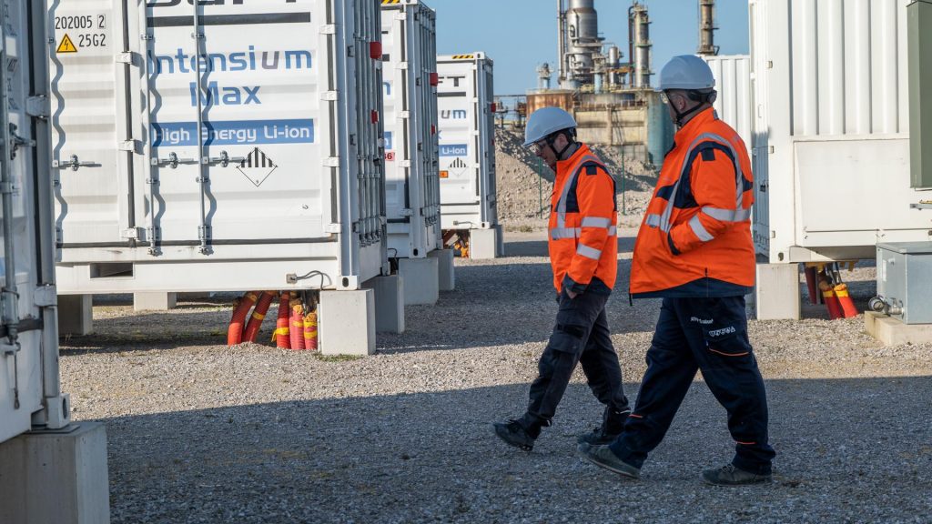 Workers walking between containerized lithiumion battery storage units at an energy storage installation.