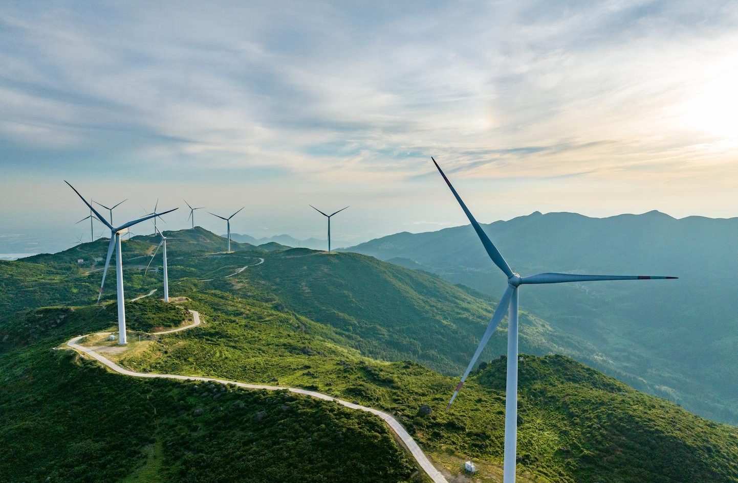 Onshore wind turbines positioned along mountain ridges in a vast green landscape.