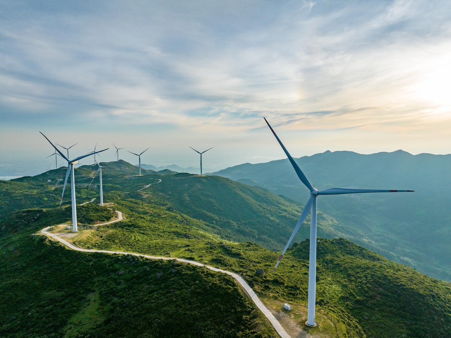 Onshore wind turbines positioned along mountain ridges in a vast green landscape.