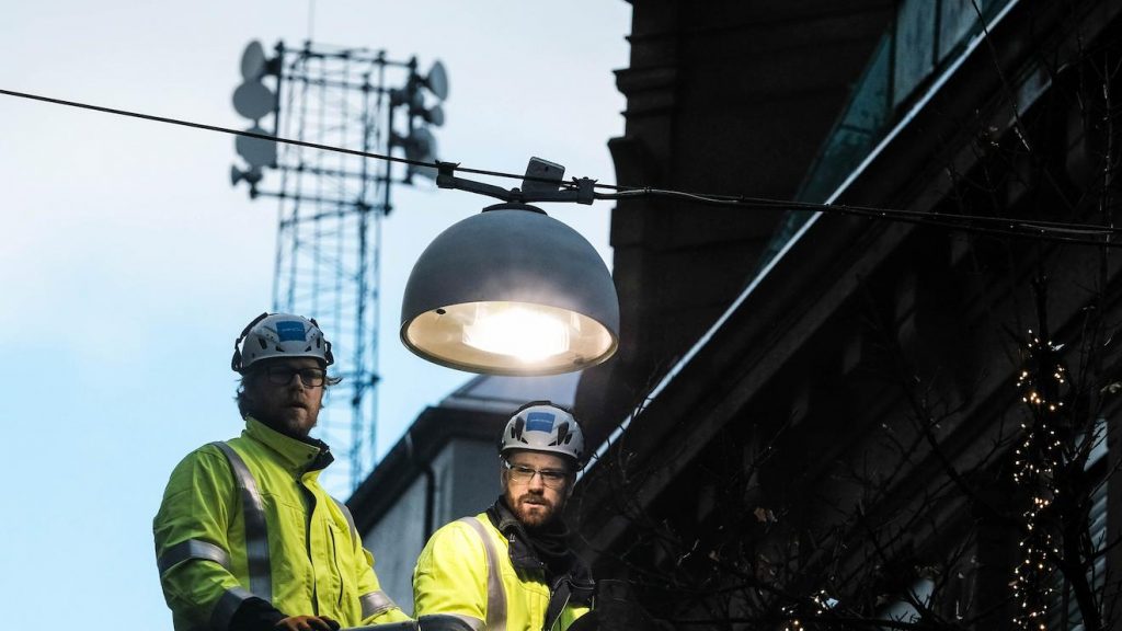Technicians installing urban street lighting using a bucket lift, maintaining public lighting infrastructure in a historic city environment