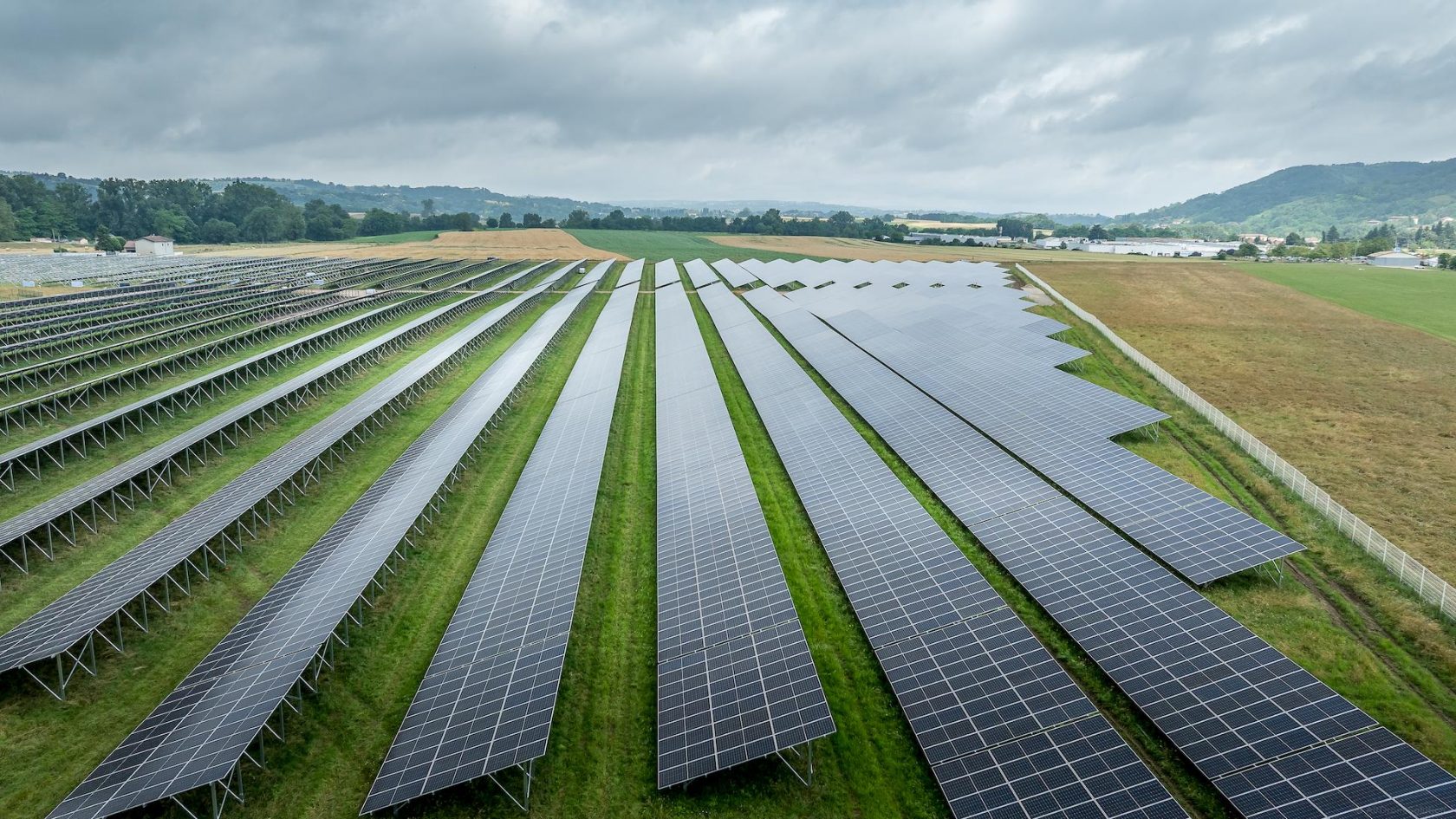 Large solar photovoltaic installation with long rows of panels across a wide green field.