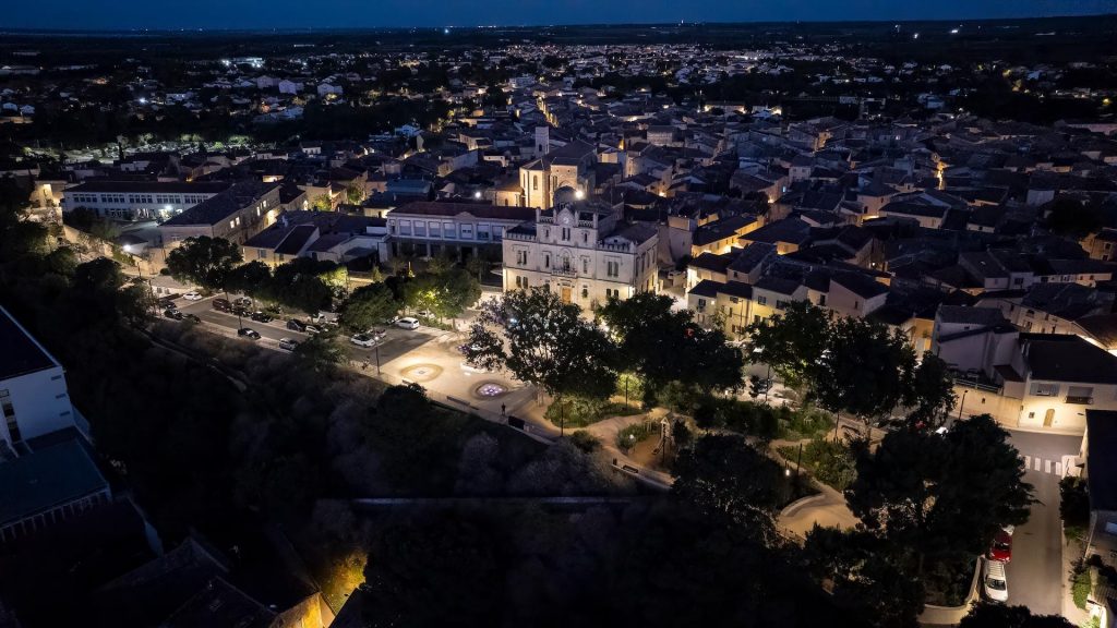 Aerial night view of Nîmes city center illuminated by public lighting, highlighting historic architecture and urban mobility