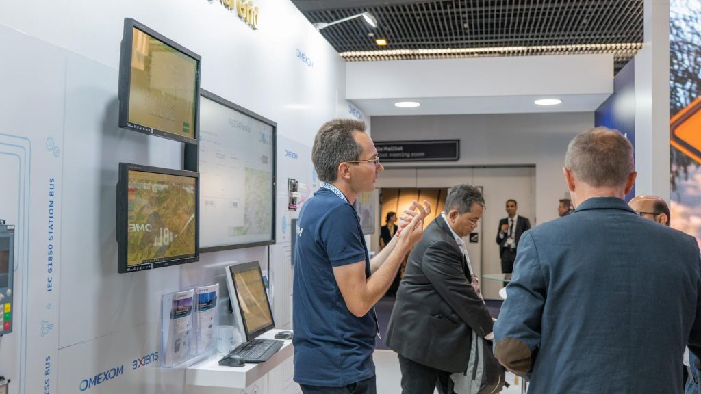 Energy industry professionals discussing digital grid monitoring solutions at an Omexom exhibition booth during a power transmission event