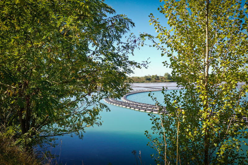 View through trees of the floating walkway connecting solar panel rows at the Saint-Élix-le-Château floating photovoltaic plant.