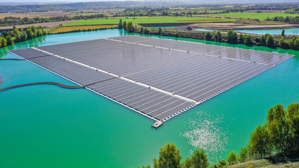 Aerial view of the floating solar array at the Saint-Élix-le-Château hybrid solar power plant, covering a turquoise quarry lake surrounded by farmland in southwestern France.