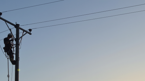 Power line technician working on a utility pole against a dusk sky.